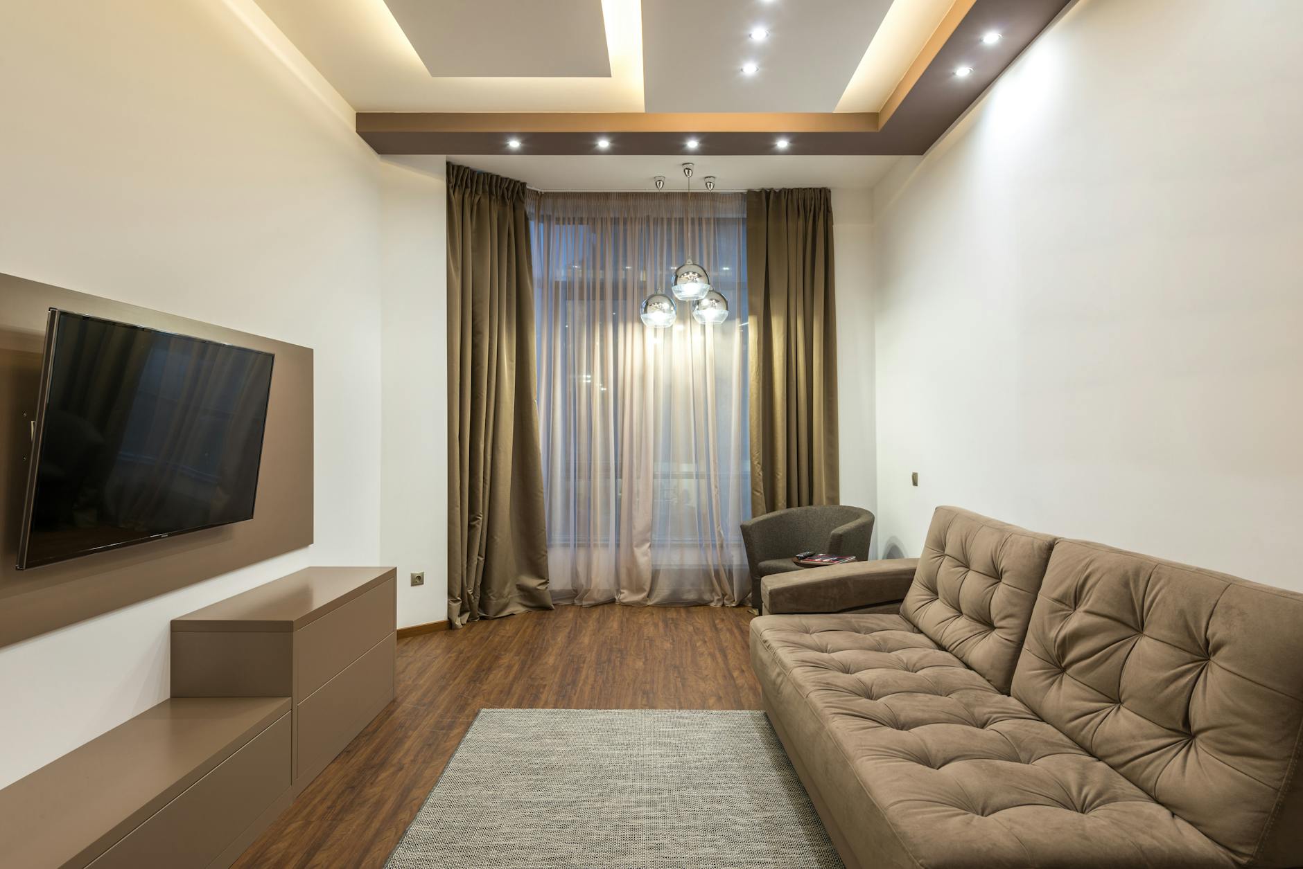 A sleek beige living room featuring a flat screen TV, sofa, and elegant lighting.
